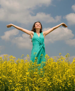 Woman wearing a green dress with her arms out, standing in a field of yellow flowers