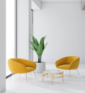 White office waiting room with two gold sitting chairs, a tall plant and a small table are between the chairs.
