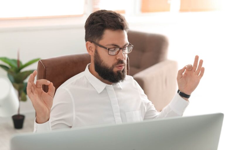 A man in office attire sitting at a desk meditating