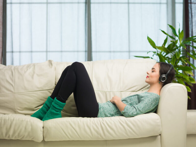 Young woman laying down on a beige couch wearing headphones